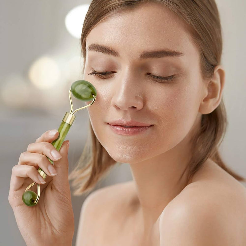 Facial jade roller with green stone and gold handle held by woman with bare shoulders and relaxed expression.